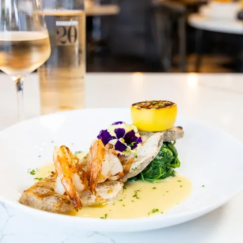 Grilled fish with spinach, shrimp, and charred lemon, served with a glass of rose wine.