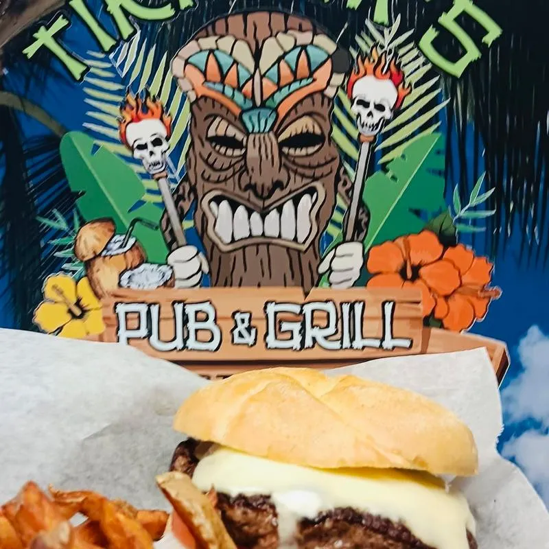 Burger and fries served on table in front of Tiki Tim's wall trademark.