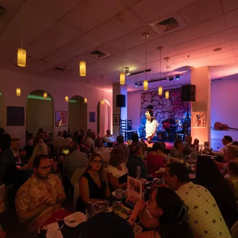 Dimly lit restaurant with a lively, crowded atmosphere, vibrant lighting and live music.