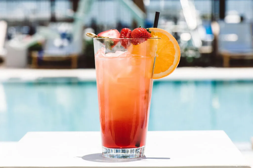 Pink tropical cocktail beside swimming pool.