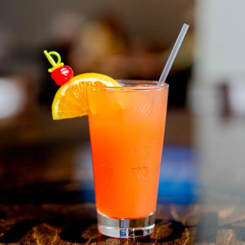Palate Punch cocktail, orange colored garnished with orange slice and cherry.