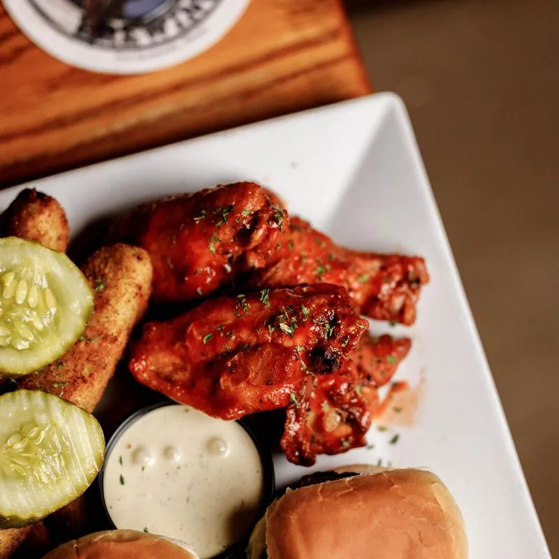 Sampler platter featuring buffalo wings, mozzarella sticks, sliders, pickles, and sauce.