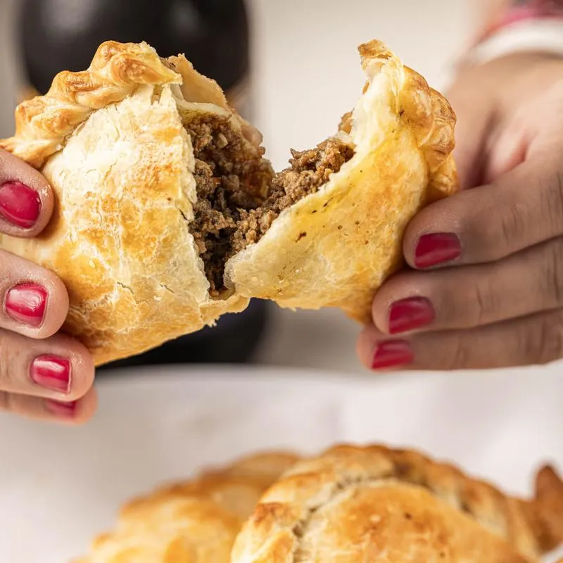 A person holding beef empanada in their hands, close up.