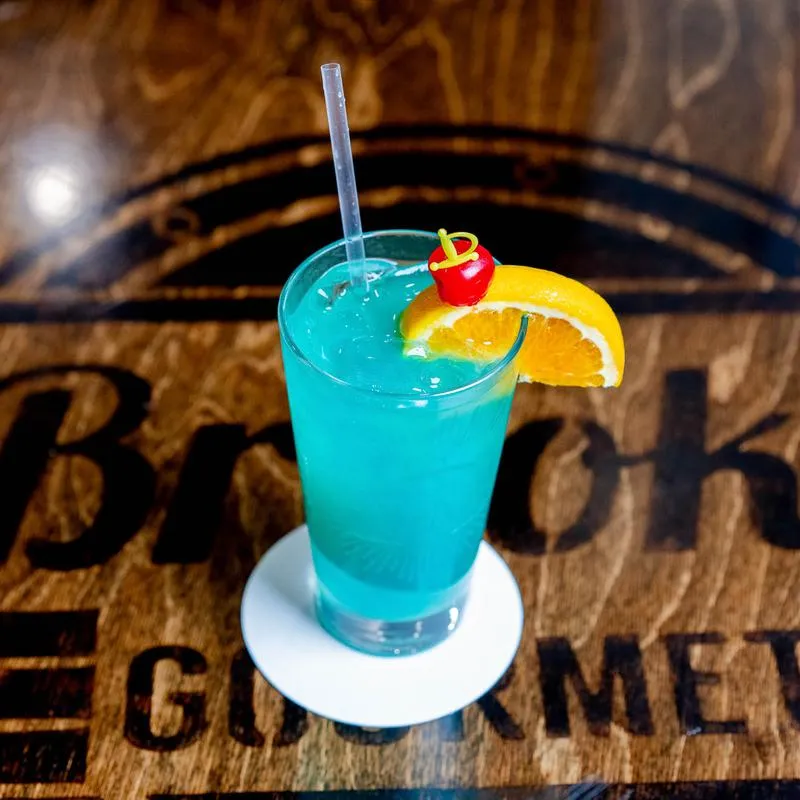 Nauti Mermaid cocktail, light blue colored with orange slice and cherry as garnish.