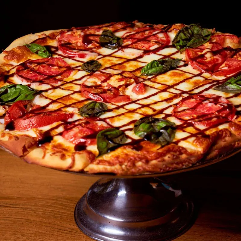 A pizza with drizzle,  tomato, basil and cheese top.