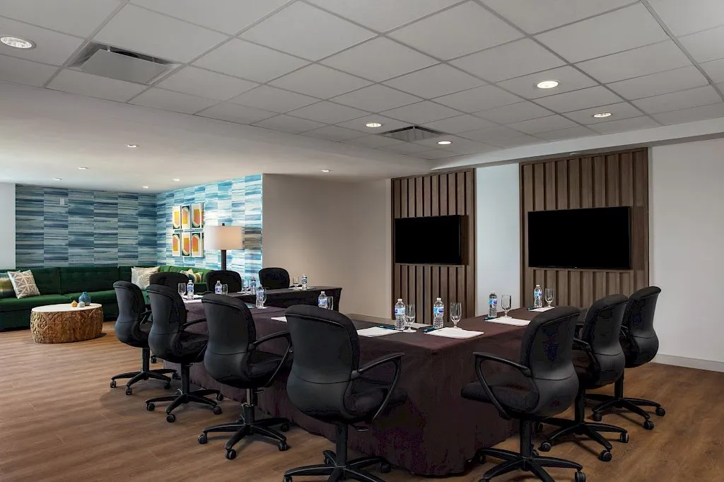 Modern conference room with a large table, chairs, and two TVs on the wall.