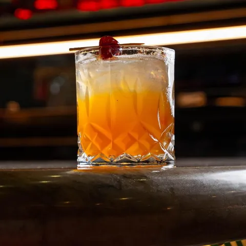 Orange cocktail served over ice with cherry.