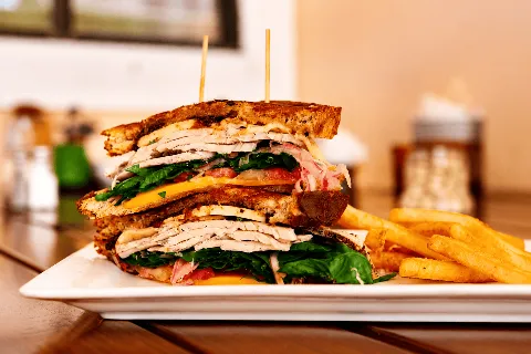 Stacked turkey club sandwich with lettuce, tomato and cheese, served with fries