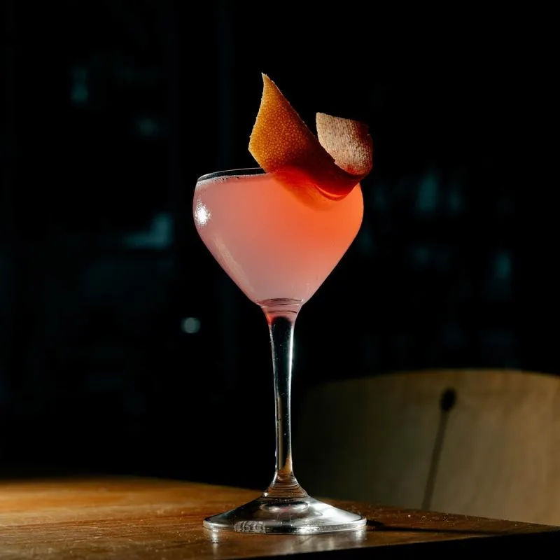Naked and Famous cocktail served in a coupe and garnished with a citrus peel.