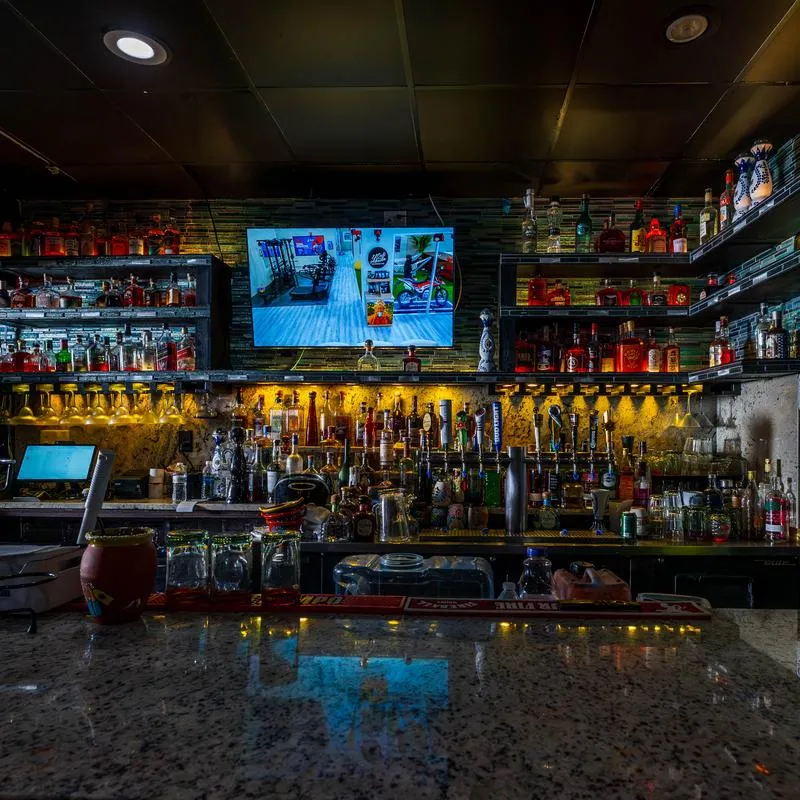 Close view at the bar with various bottles on the shelves and TV screen.