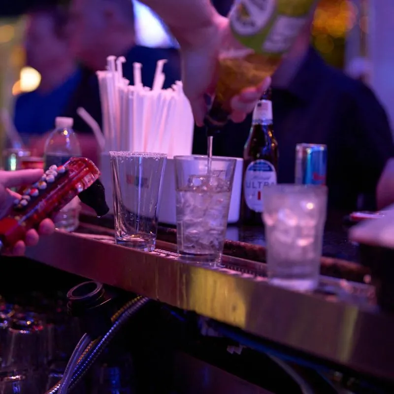 Bartender pouring liquor into a glass with straws nearby on the bar counter.