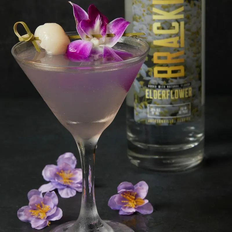 Violet Tendencies cocktail with lychee and orchid garnish.
