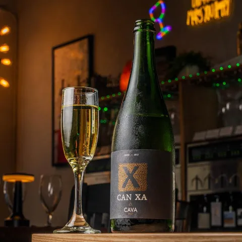 Sparkling wine bottle  and a filled flute glass sit on a wooden bar counter.