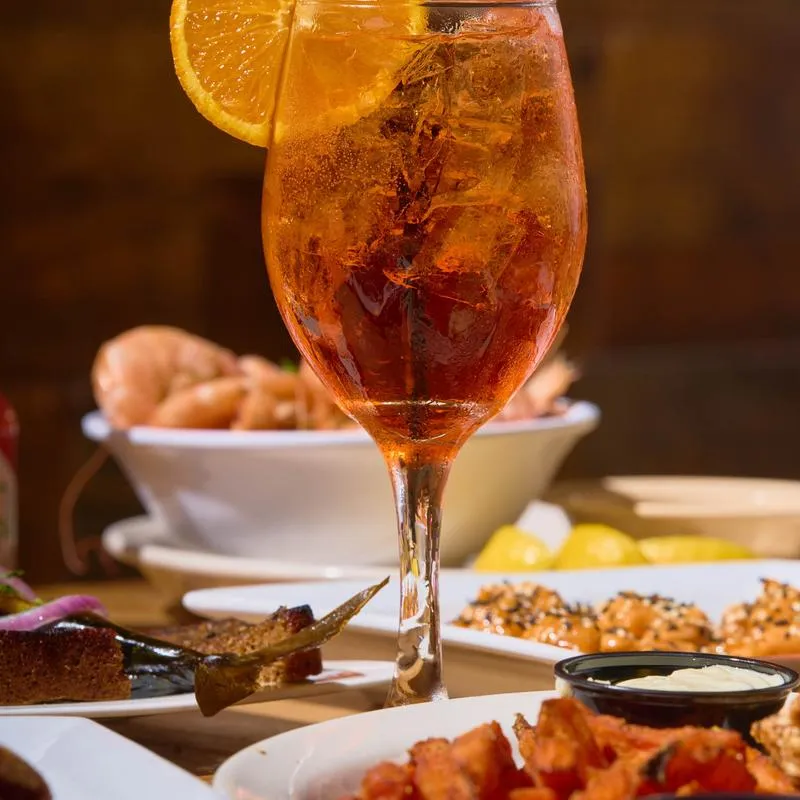 Aperol Spritz served in a wine glass alongside various dishes.
