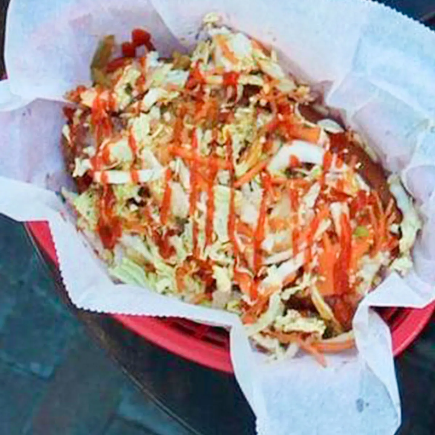 Basket of food topped with shredded lettuce, sauce, and sliced vegetables—featuring the signature Kogi Dog—all served on parchment paper.