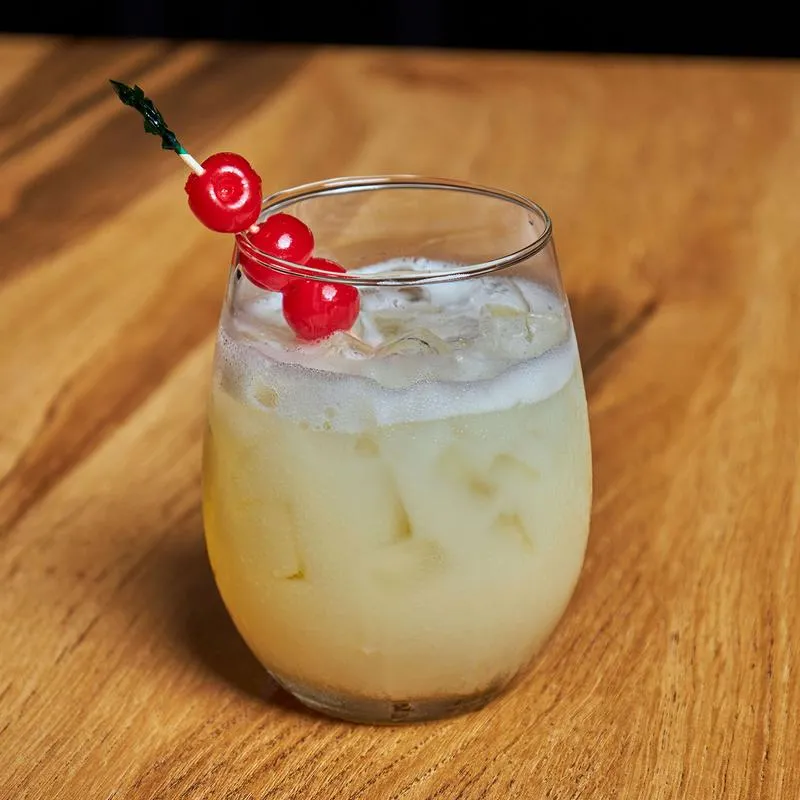 A white colored cocktail garnished with cherries.