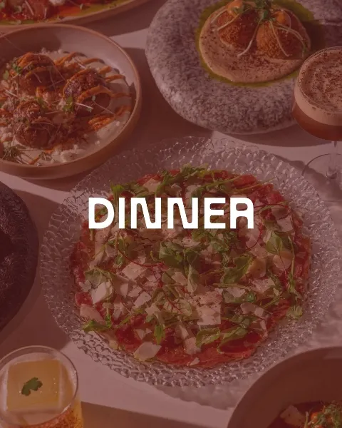 A variety of dishes on a table, including a pizza topped with greens, a bowl of meatballs with sauce, and other plates of food; the word 'DINNER' is overlaid on the image.