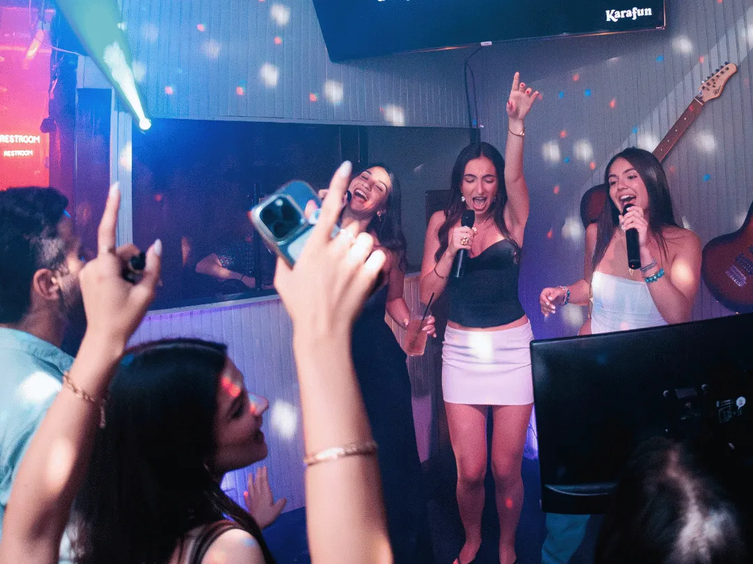 Three women singing karaoke on stage. Ladies Night flyer for Sweet Caroline Wynwood — free drinks for women every Wednesday from 8PM to 11PM