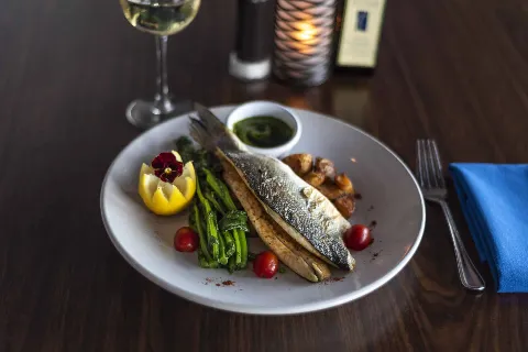 Whole roasted branzino with crispy skin, served with grilled asparagus, cherry tomatoes, roasted potatoes, and herb salsa verde