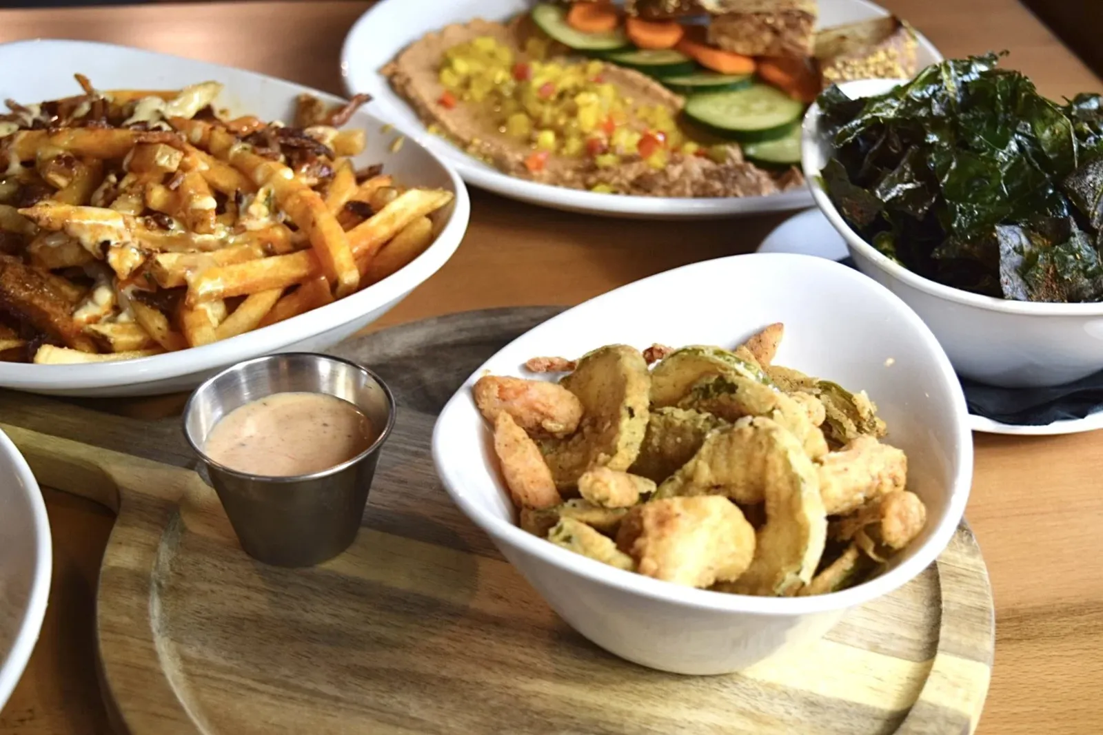 Assorted food dishes including French fries with cheese, fried vegetables, salad with cucumber and carrots, seaweed, and a dish with chopped meat and vegetables, on a wooden serving board.