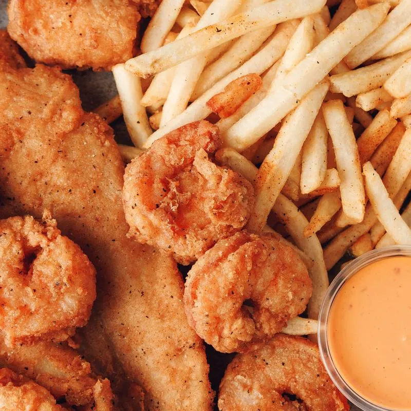 A plate of fried fish and shrimp served with french fries and special sauce.