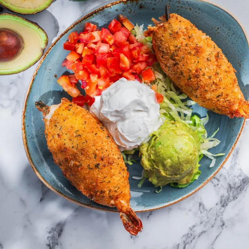 A plate of Mexican food features breaded shrimp, guacamole, salsa, and sour cream.
