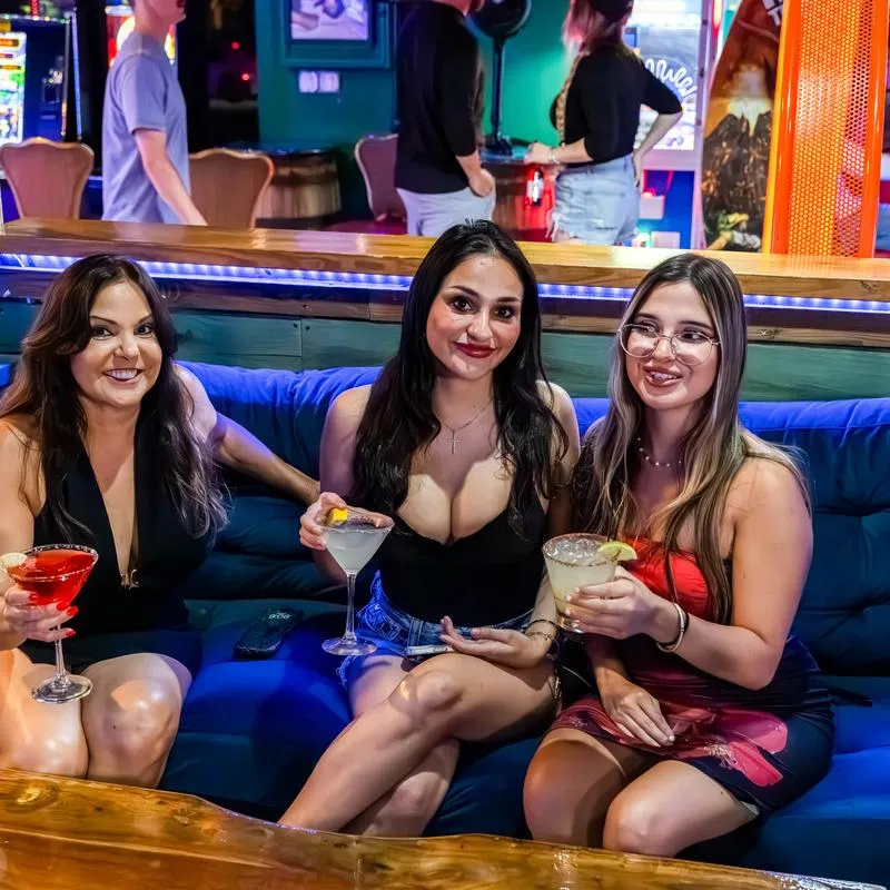 Three people sitting together on a blue couch, holding cocktails.
