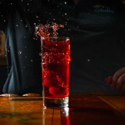 Cherry being dropped into a colins glass with a cocktail.