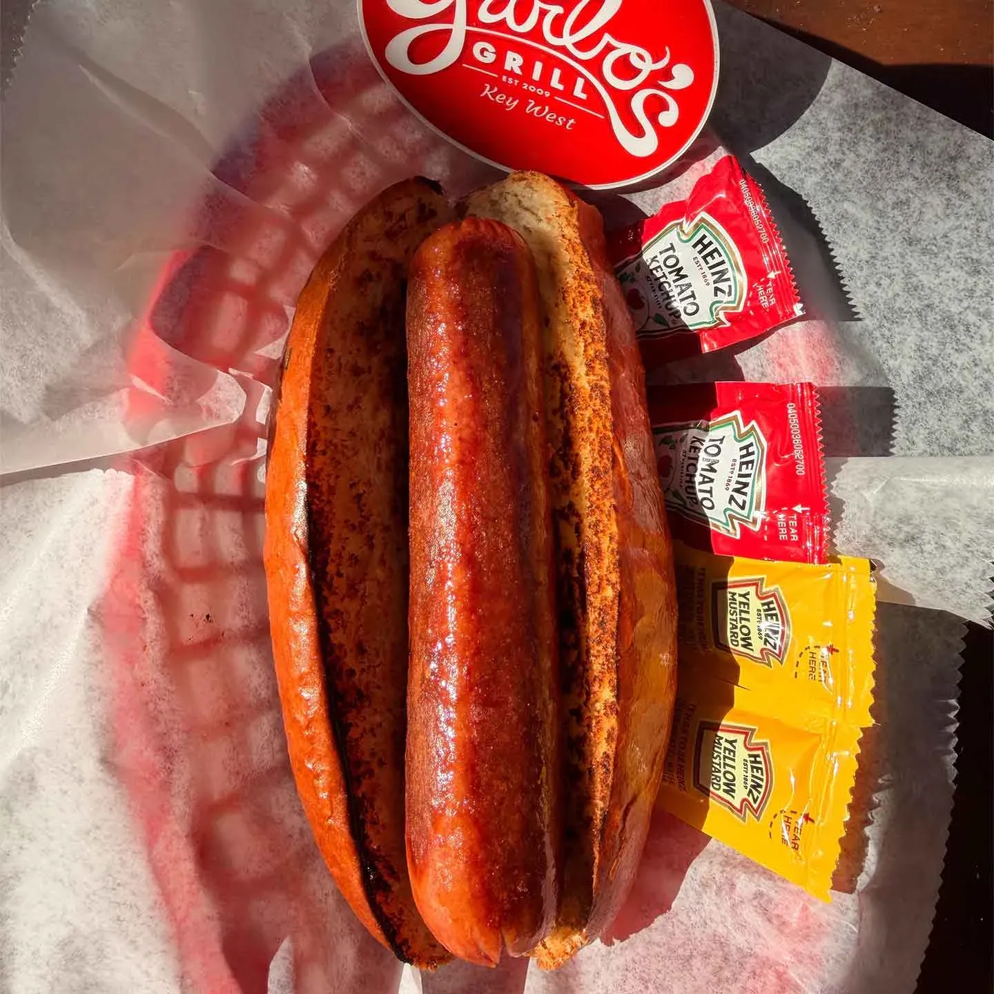 Grilled hot dog on a toasted bun with ketchup and mustard packets on the side.
