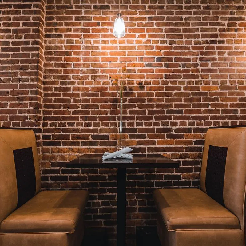 A small booth in a restaurant, with a brick wall behind it, with a hanging light.