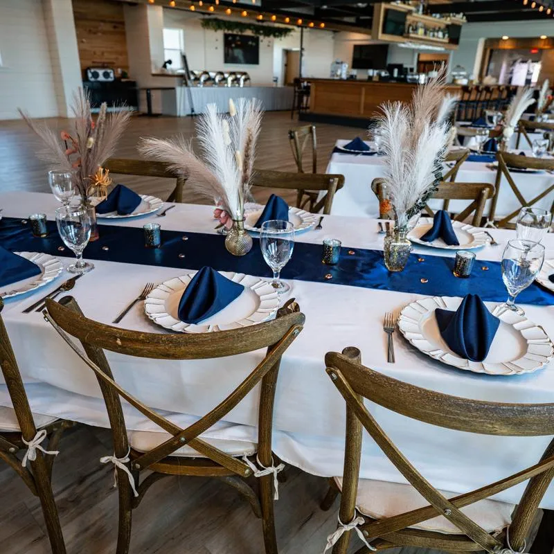 Interior, tables set with blue runners, white chargers and pampas grass centerpieces.
