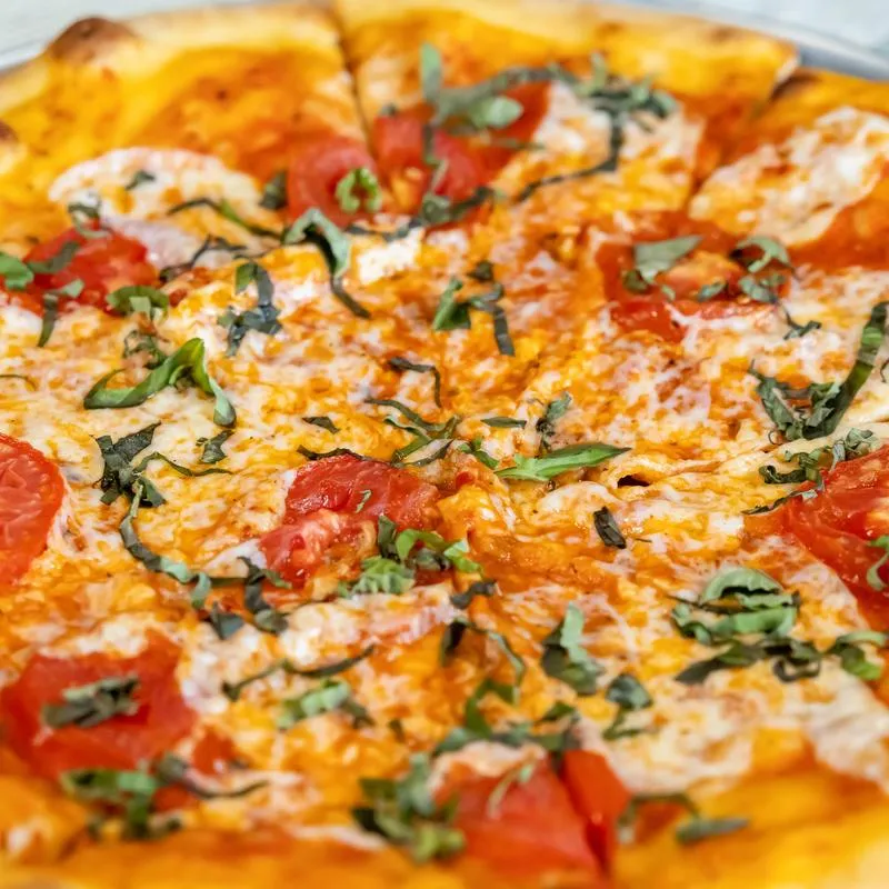Margherita pizza topped with tomato slices and basil, close-up.