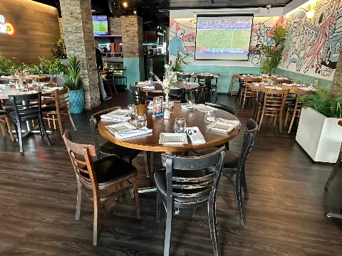 A round table set for a group in the dining room, with the mural and the TVs behind