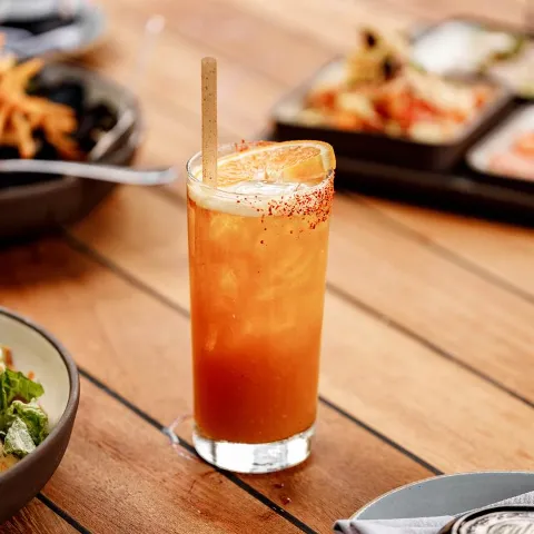 A cocktail drink served on a wooden table, surrounded by assorted food dishes.