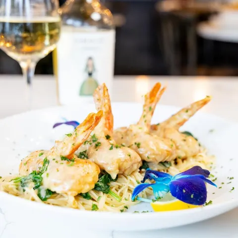 Creamy shrimp pasta with herbs and orchid garnish, served with white wine.