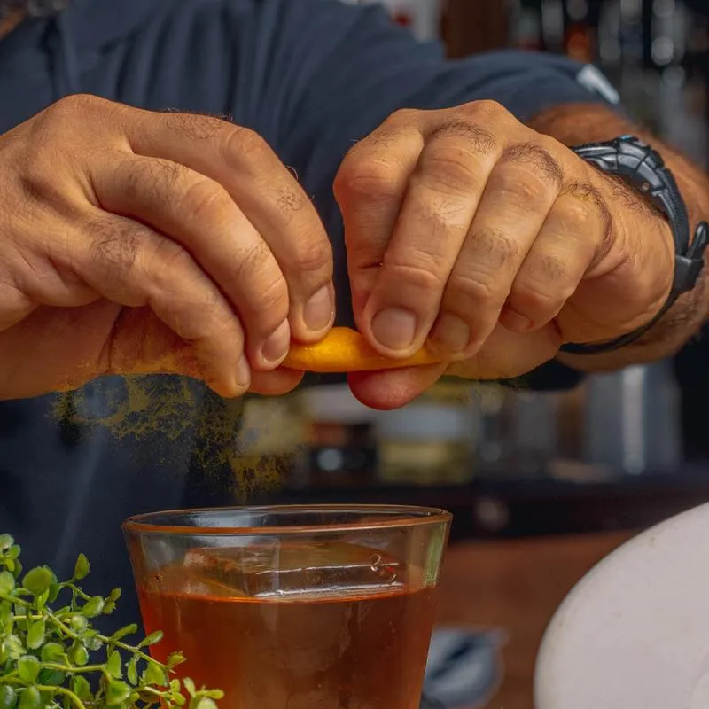 Hands squeezing a slice of fruit into a cocktail.