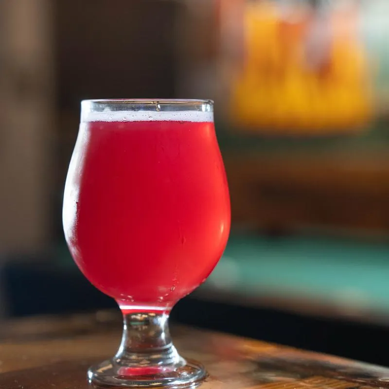 Pink fruit beer in a tulip glass on a counter.