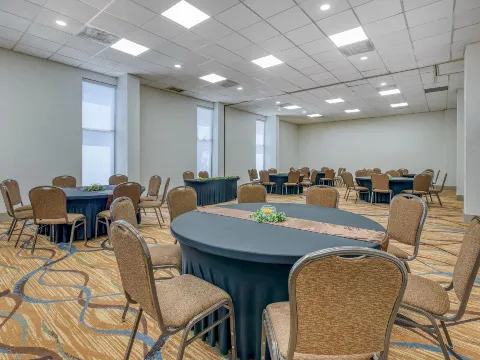 A conference room with round tables and chairs arranged for an event, featuring a patterned carpet and a white ceiling.