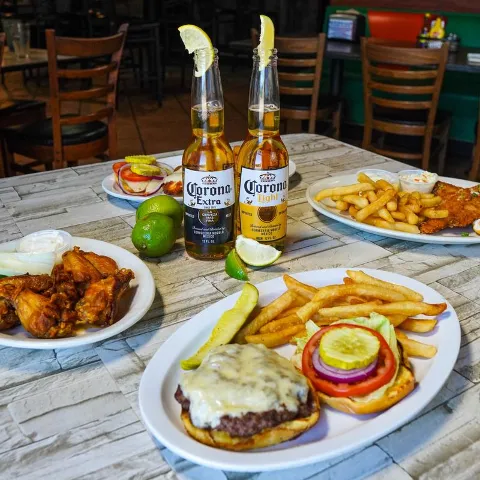 Burger with fries, chicken wings, and beer bottles on a restaurant table.