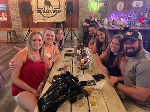 A group of people sit around a long wooden table inside a bar labeled