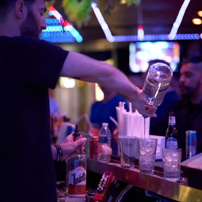 Bartender filling a glass of ice with liquor at the bar counter.