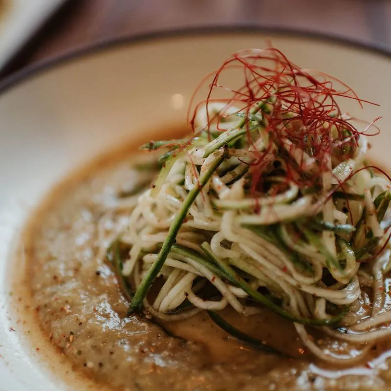 A dish of noodles served in a sauce and topped with shredded vegetables.