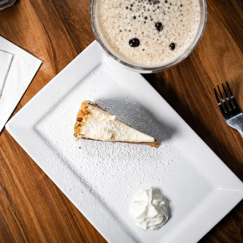 Slice of carrot cake garnished with whipped cream, served alongside Espresso Martini.