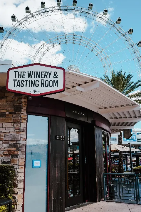A storefront with a sign that reads 'The Winery & Tasting Room' in front of a large Ferris wheel.