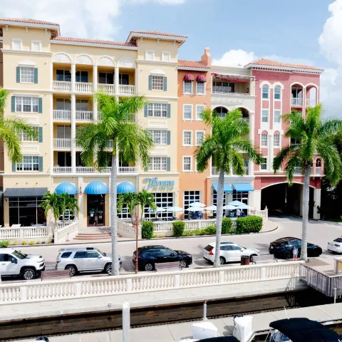 Streetscape with colorful buildings, palm trees, and parked cars on a sunny day.