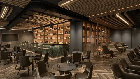 Modern bar and lounge with dark wood paneling, a marble-topped bar counter, and seating area with black chairs, small tables with drinks, and wooden shelving with bottles in the background.