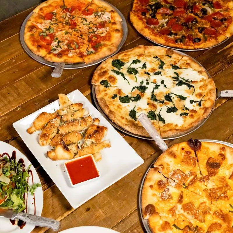 Various whole pizzas served on the table alongside a plate of Garlic Twists.