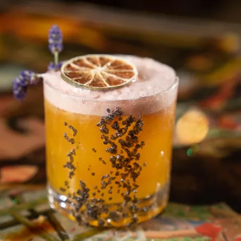 Smoked cocktail drink garnished with lavender and dehydrated citrus wheel