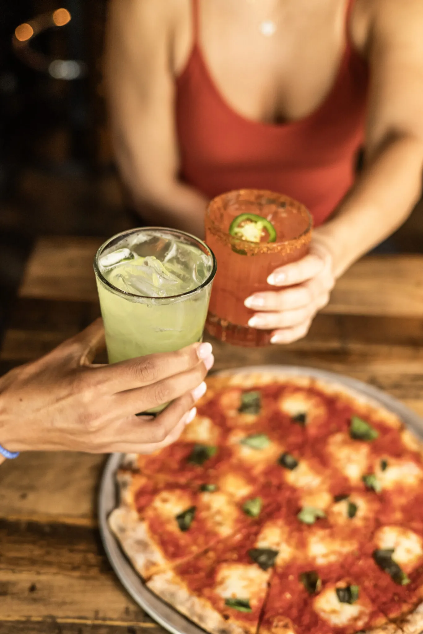 Two drinks clinking over a pizza